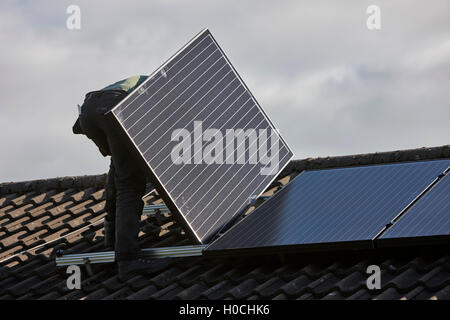 man installing rooftop solar panel array in a domestic solar panel installation in the uk Stock Photo