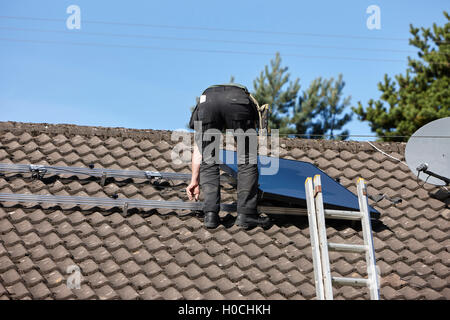 man installing rooftop solar panel array in a domestic solar panel installation in the uk Stock Photo