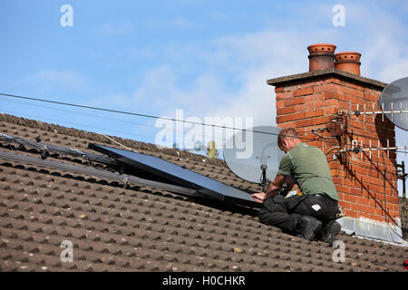 man installing rooftop solar panel array in a domestic solar panel installation in the uk Stock Photo