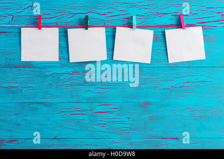 Four blank white notepads hanging from cotton by colorful wooden clothespins over blue wood panel background with crackle paint Stock Photo