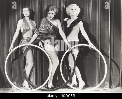 Three scantily clad women holding large rings Stock Photo