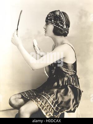 Side view of young woman holding powder puff and mirror Stock Photo