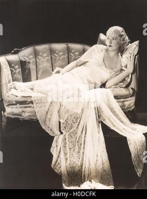 Woman in lace gown lounging on sofa Stock Photo