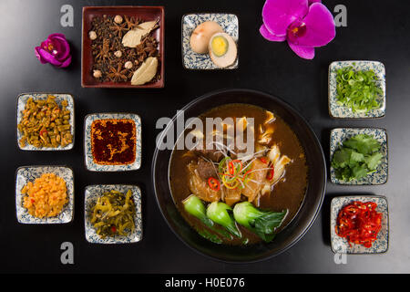 Oriental beef noodles with garlic, chili sauces, egg and herbs on black table Stock Photo