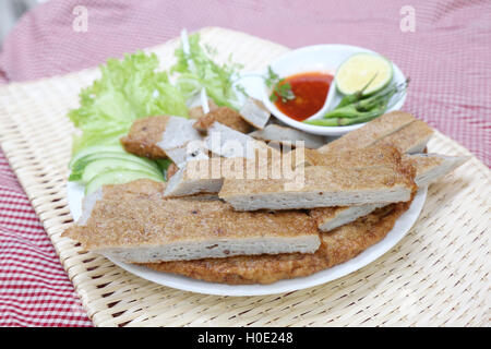Vietnamese fish paste cake or cha ca on white plate with herbs, cucumber, lemon, chili and sauce on bamboo tray Stock Photo