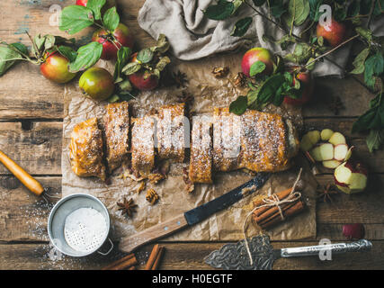 Apple strudel cake with cinnamon and sugar powder cut in slices served with star anise, nuts and fresh apples on rustic wooden b Stock Photo