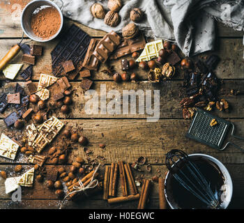 Background with chocolate. Pieces of white, dark and milk chocolate, nuts, cocoa powder, melted chocolate in bowl and spices. Ho Stock Photo
