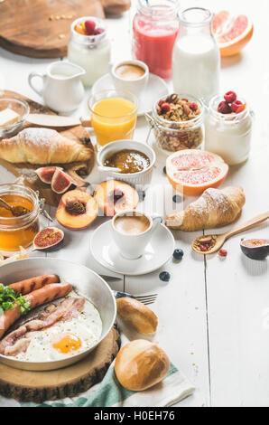 Fried egg with sausages and bacon, bread, croissants with jam and butter, fruits, smoothie, orange juice, yogurt, granola with m Stock Photo