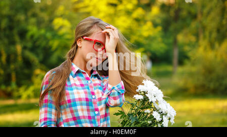 Young girl straightens her hair in a city park. She is holding a bouquet of daisies. Outdoor Activities on a sunny day. Stock Photo