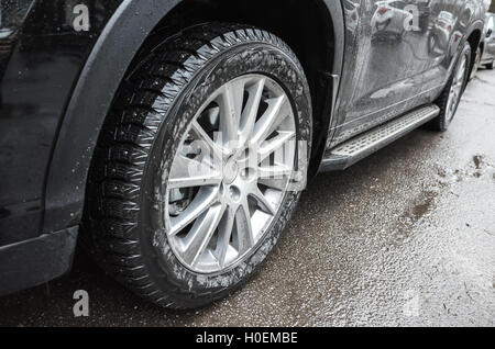 Fragment of black unidentifiable suv car, light alloy wheel with winter tires on dirty road Stock Photo