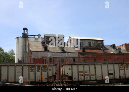 Lynchburg, Virginia, USA. Cargo train passing by the abandoned Piedmont Flour Mill and Silo buildings on Jefferson Street. Stock Photo