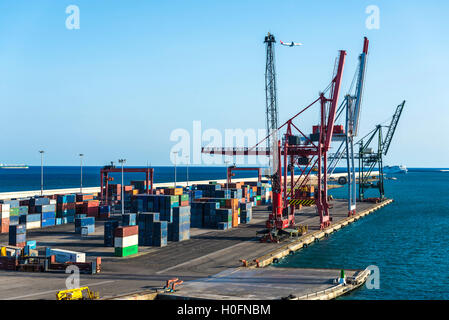 Cranes at the port surrounded by containers while passing a cruise ship, a tanker and a plane in Barcelona, Catalonia, Spain Stock Photo