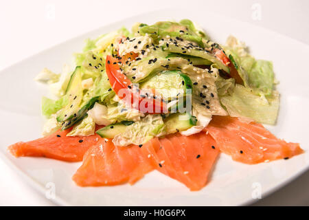 Salad with salted salmon, tomatoes and cucumbers on a green cushion with nut mix with sesame sauce Stock Photo