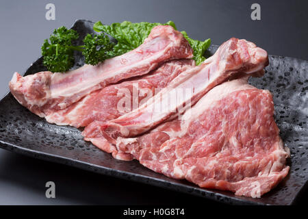Fresh bone in pork ribs with lettuce on black dish Stock Photo