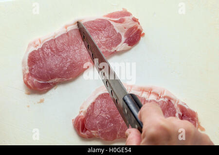 Cutting fresh raw beef with knife in the kitchen Stock Photo