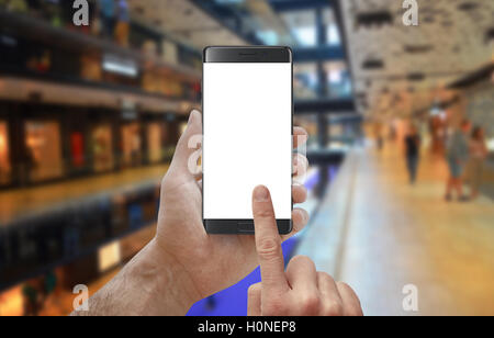 Using smart phone in shopping mall. Man holding phone with isolated display for mockup. City shopping center in background. Stock Photo