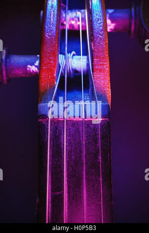 Studio composition of an old dusty violin, blue and purple illumination from aside, closeup view on nut and pegbox. Stock Photo