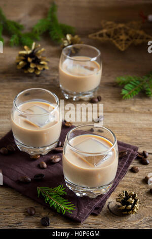 Irish cream coffee liqueur with ice, Christmas decoration and ornaments over rustic wooden background - homemade festive drink