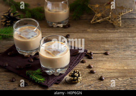 Irish cream coffee liqueur with ice, Christmas decoration and ornaments over rustic wooden background - homemade festive drink