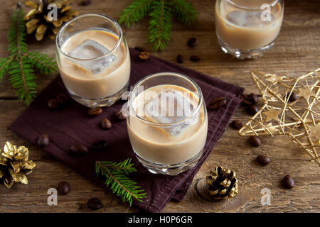 Irish cream coffee liqueur with ice, Christmas decoration and ornaments over rustic wooden background - homemade festive drink Stock Photo