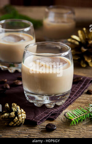 Irish cream coffee liqueur with ice, Christmas decoration and ornaments over rustic wooden background - homemade festive drink