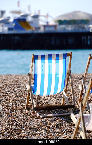 a single empty deckchair on a pebbly beach facing the sea and a pier Stock Photo