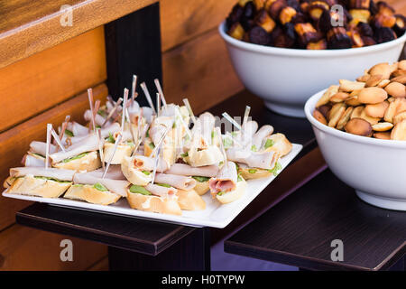 Wood brown tables full of different snacks for party or wedding celebration. White plates with cheese sandwiches and variety of Stock Photo