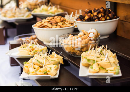 Wood brown tables full of different snacks for party or business conference. White plates with cheese sandwiches and variety of Stock Photo