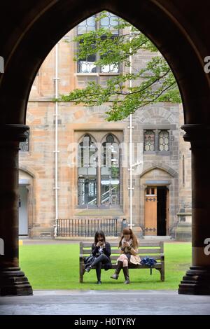 Students using mobile phones seated in the grounds of Glasgow University, Scotland, UK Stock Photo
