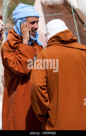 Atlas Mountains, Morocco.  Market Scene in Village near Dades Gorge.  Two Berber Men Talking, One Using Cell Phone. Stock Photo