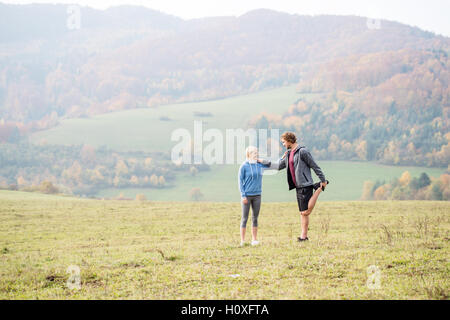 Two young beautiful runners in autumn nature, stretching legs Stock Photo
