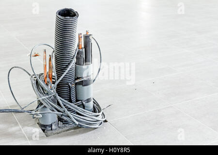 Bunch of various electric cables in corrugated pipe is coming out from the tiled floor, ready to be connected into power unit. Stock Photo