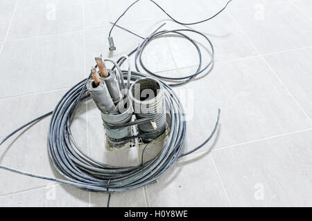Bunch of various electric cables in corrugated pipe is coming out from the tiled floor, ready to be connected into power unit. Stock Photo