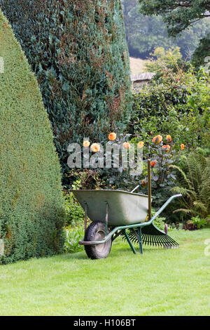 Wheelbarrow, lawn rake and trowel ready for work in a large garden Stock Photo