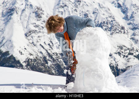 Nice looking pretty blonde caucasian happy cheerful succesful girl staying at the top of mountain making snowman Stock Photo