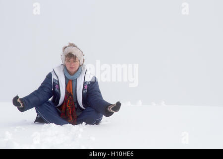 Nice looking pretty blonde caucasian happy succesful girl sitting in the zen pose at the top of mountain covered by snow Stock Photo