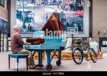 Man plays piano towed by bicycle  Keys to the Streets Piano, Woodward’s Atrium, Vancouver,  British Columbia, Canada Stock Photo