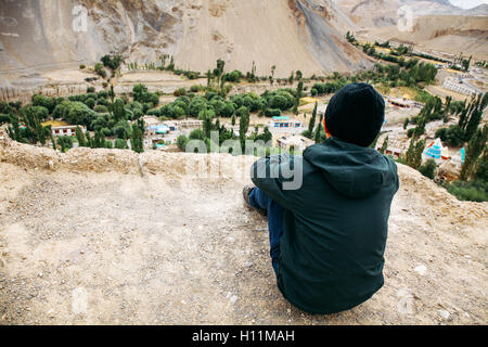 Young male traveler sitting on the sand cliff, thinking about something in Leh, Ladakh, India Stock Photo