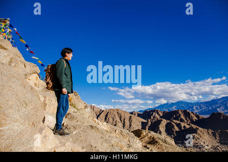 Young Asian traveler standing on high hills and looking away at the village over blue sky background in Leh, Ladakh, India Stock Photo