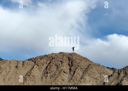 Winning and happy people jumping on the top of mountain peak in blue sky. Stock Photo