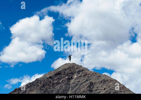 Winning and happy people jumping on the top of mountain peak in blue sky. Stock Photo