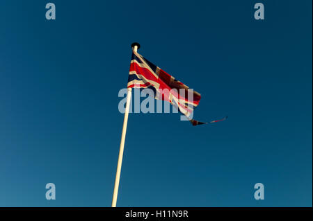 Tattered Union Jack flag against blue sky Stock Photo