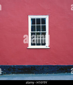 Single white framed window set against a red painted house brickwall Stock Photo