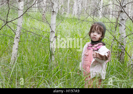 little girl stands in the grass among birches Stock Photo