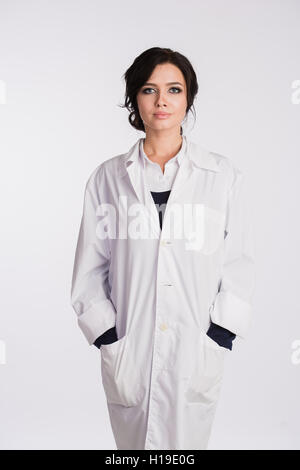 Smiling medical doctor woman with hands in pockets of robe looking at camera isolated on white Stock Photo