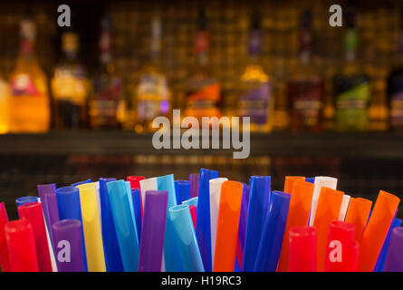 Colorful Straws and Blurred Bottles of Spirits and Liquor in the Bar at Night Stock Photo