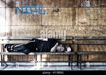 Homeless Man Sleeping on the Wooden Bench in the Train Station Stock Photo