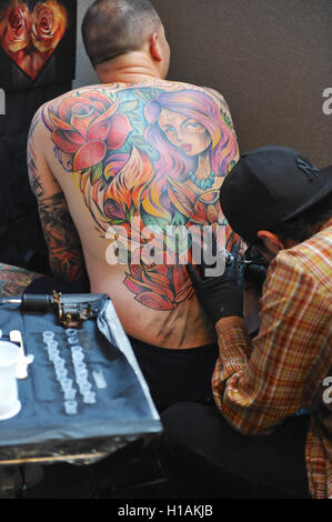 London, UK. 23rd September, 2016. A tattooist at work at the the 12th London International Tattoo Convention, which opened today in Tobacco Dock, east London.  The show features over 400 of the world’s finest, most prestigious and elite tattoo artists as well as a showcasing alternative culture in the form of piercing, burlesque and the Miss Pin Up UK competition. Around 20,000 people will attend over the weekend. Credit:  Michael Preston/Alamy Live News Stock Photo