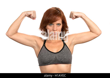Thin freckled redheaded woman flexes her bicep muscles while wearing a sports bra. Stock Photo
