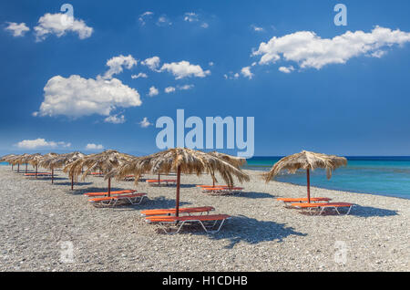 Straw umbrella on a sandy beach in Greece. Beach chairs with umbrellas on a beautiful beach in Crete island. Stock Photo
